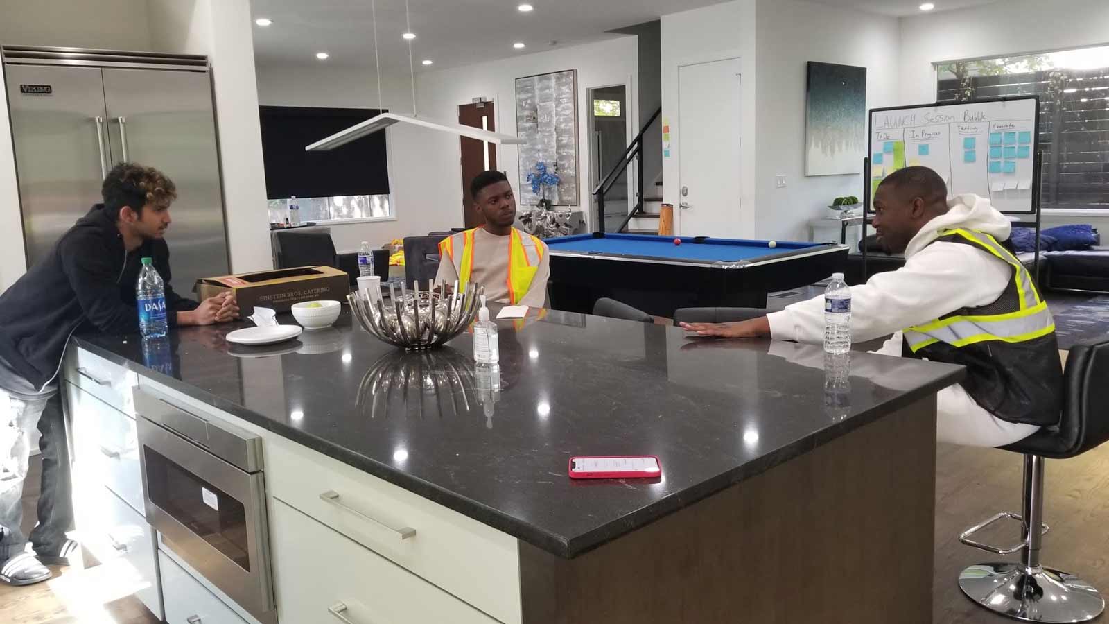 Three people discussing things around a kitchen island